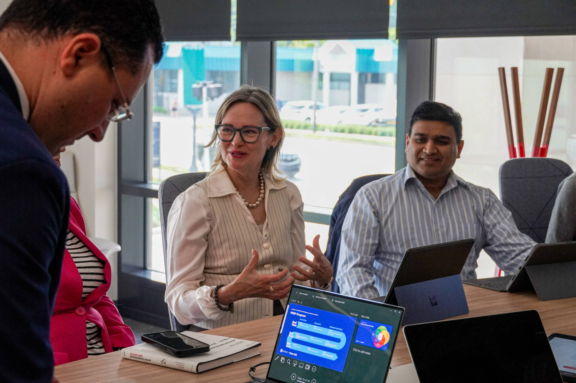 Jennifer Wangler, vice president of technology at The Right Place, gestures while speaking during a collaborative meeting. Seated beside her is another participant with a laptop open. The discussion takes place in a bright, modern conference room.